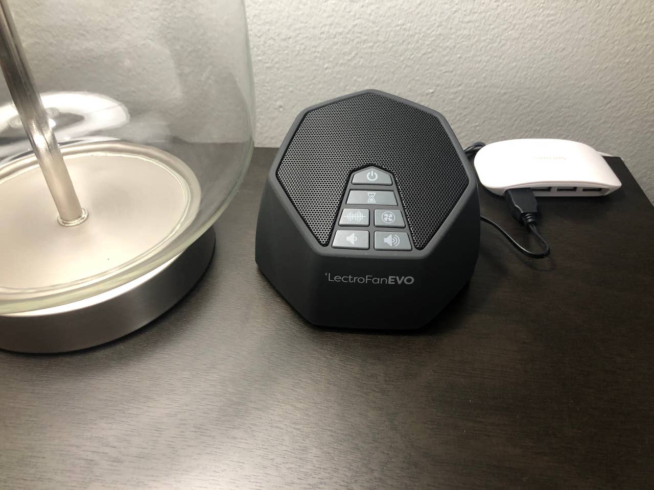White noise machine for light sleepers and multi plug USB charger on bedroom night stand.