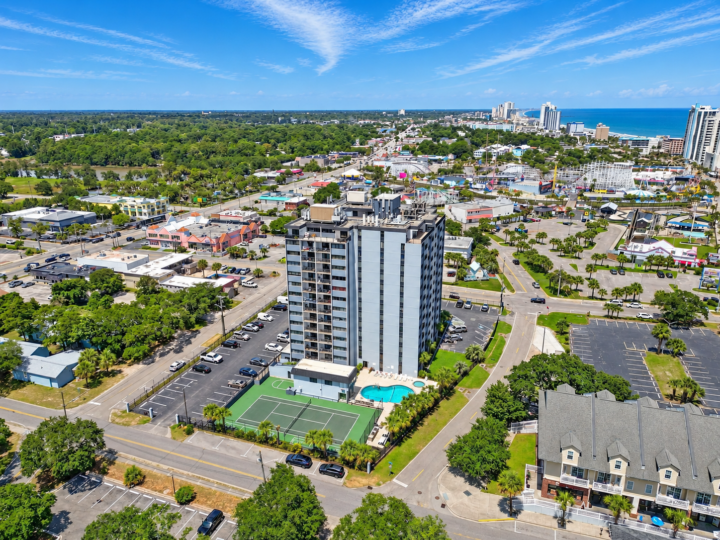 Aerial view of Holiday Towers with shared pool, hot tub, sports court, parking, and Myrtle Beach attractions nearby.
