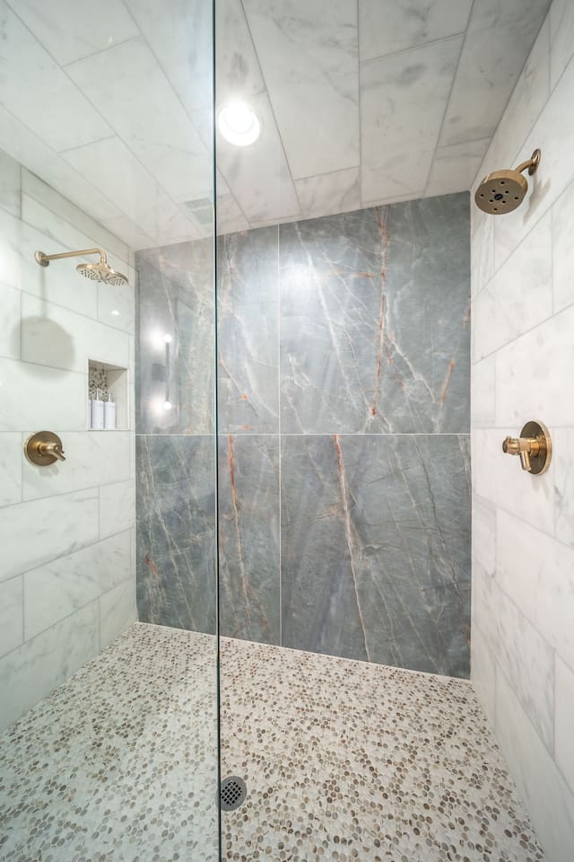 Luxury ensuite bathroom with brass fixtures, and a large spa-style walk-in shower with glass enclosure and floor-to-ceiling stone tile. Plus, heated marble floors! 