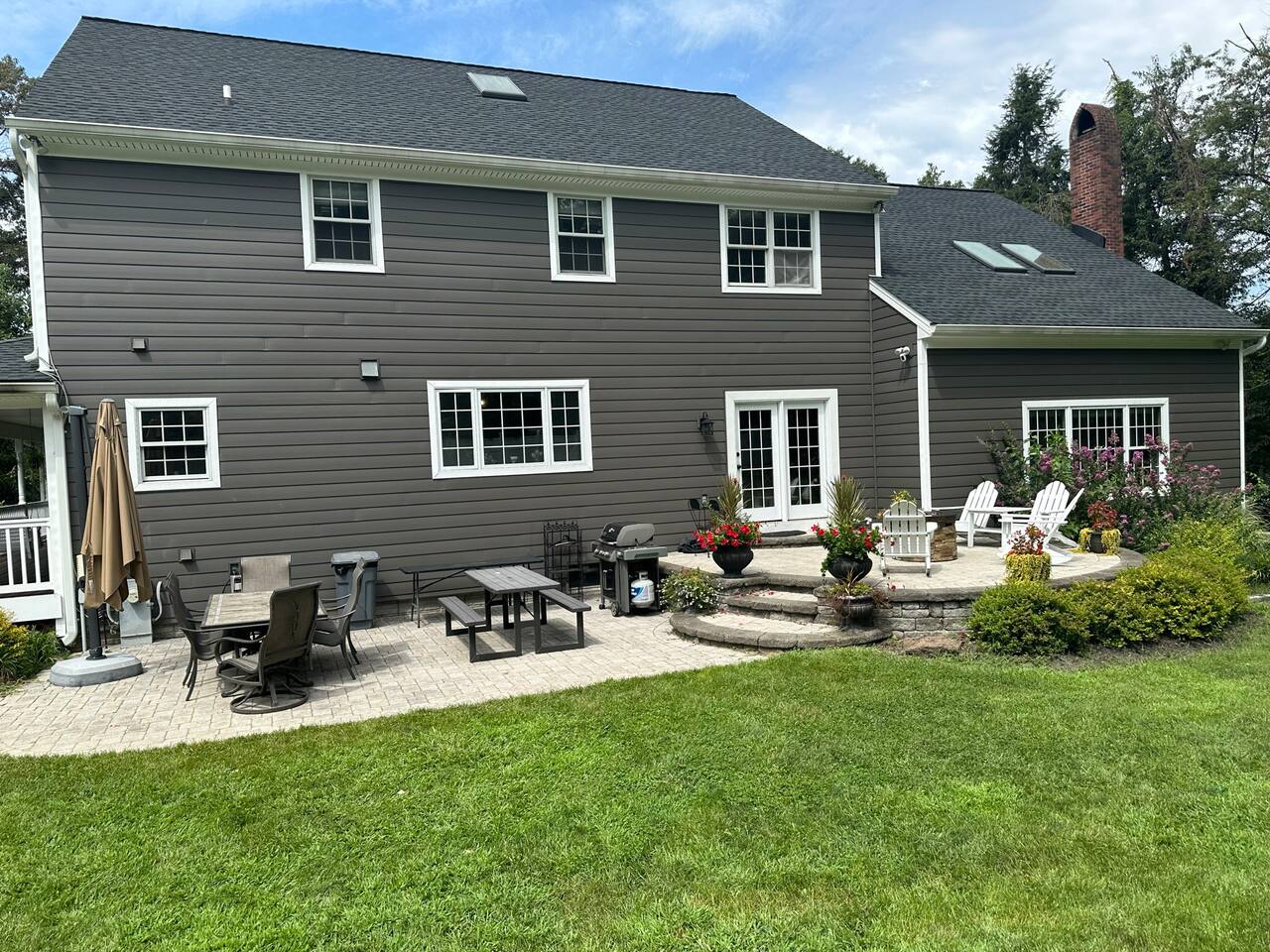 Back of the house. See multiple dining tables,  large grill, firepit, and large cantilever umbrella which provides lots of shade from the sun when extended. 