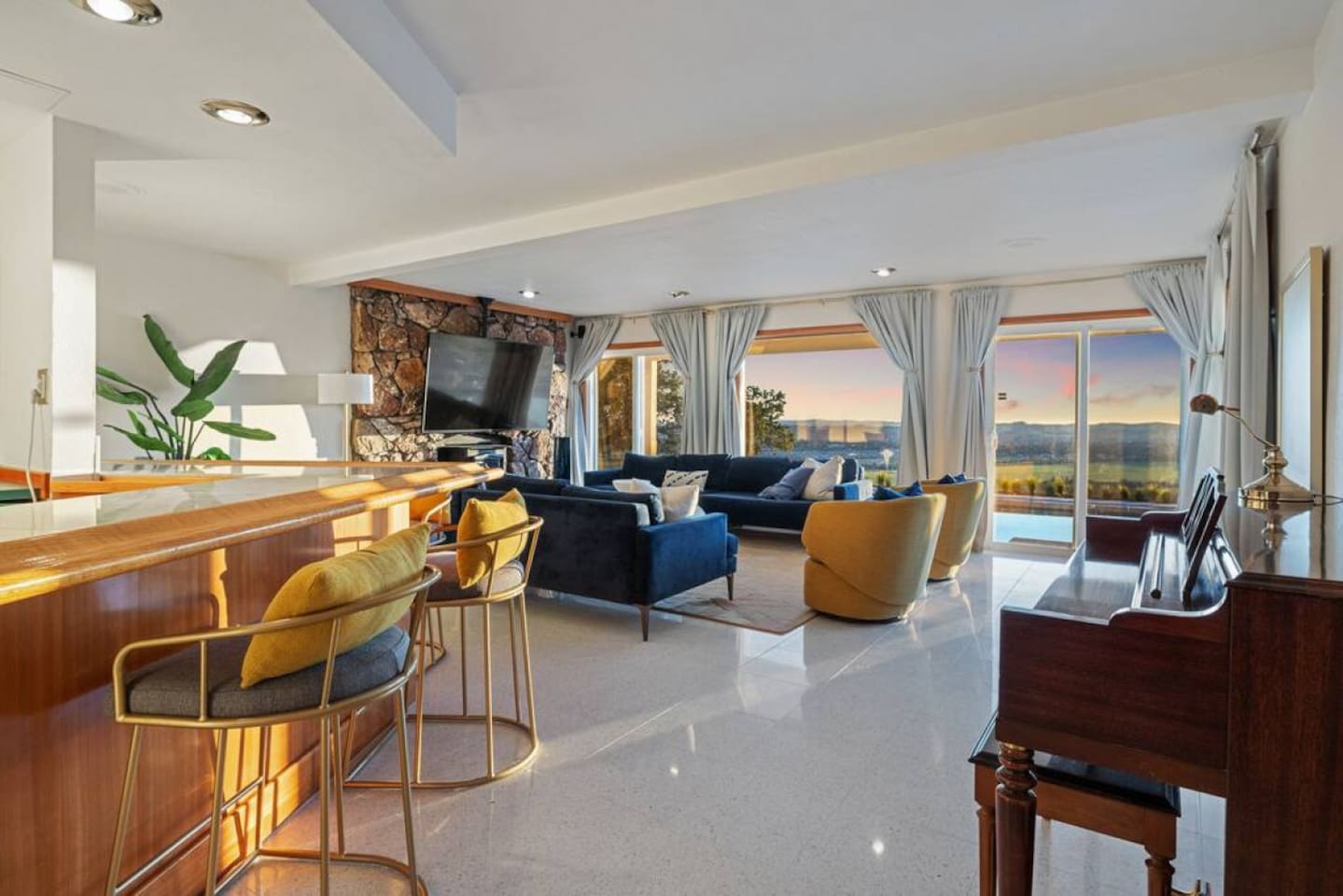 Living room with couch seating for 10, 75" 4K TV, bar, piano, and half bathroom. The living room is just inside from the pool and hot tub deck.