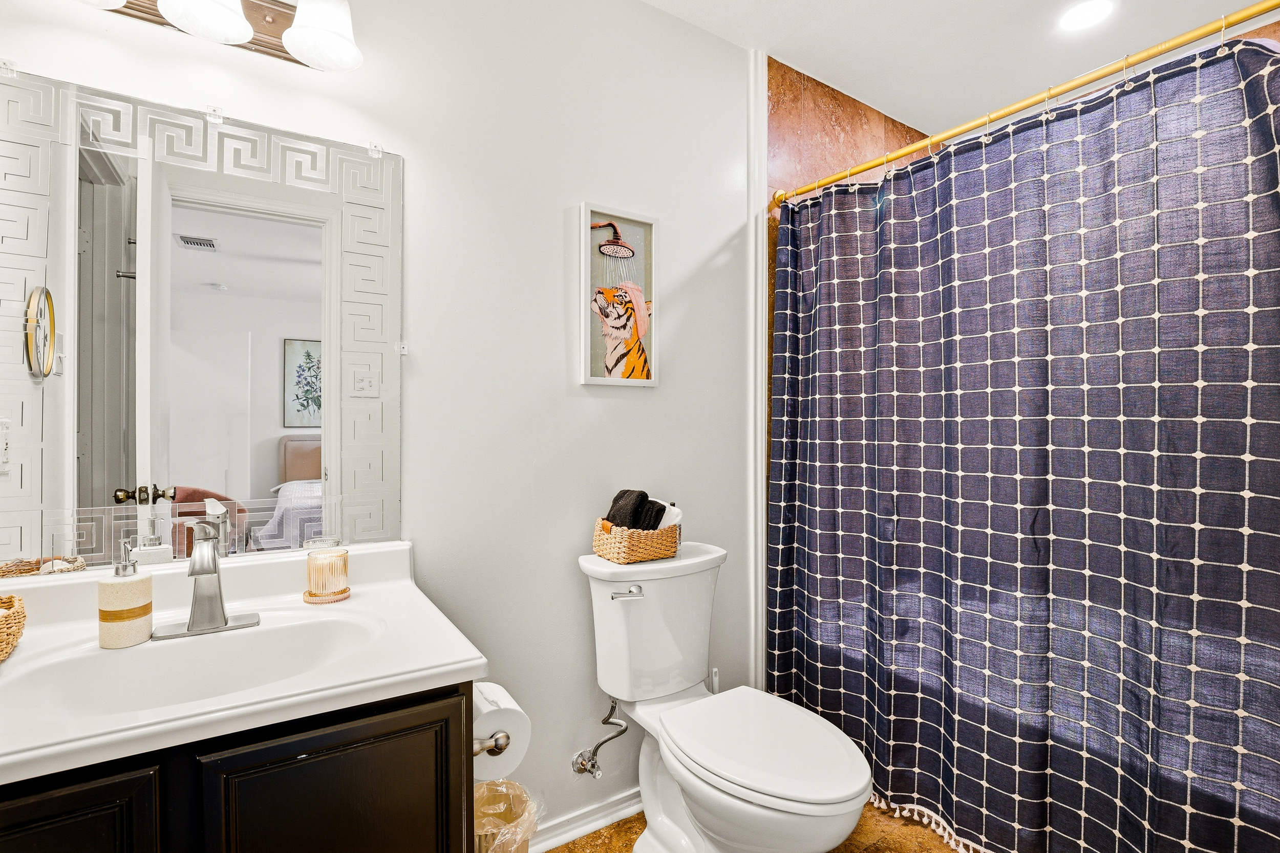 Full bathroom with tiled shower and tub combo, gold curtain rod, decorative framed mirror, and dark wood vanity. Stocked with Ginger Lily Farms shampoo, body wash, conditioner, and fresh towels.