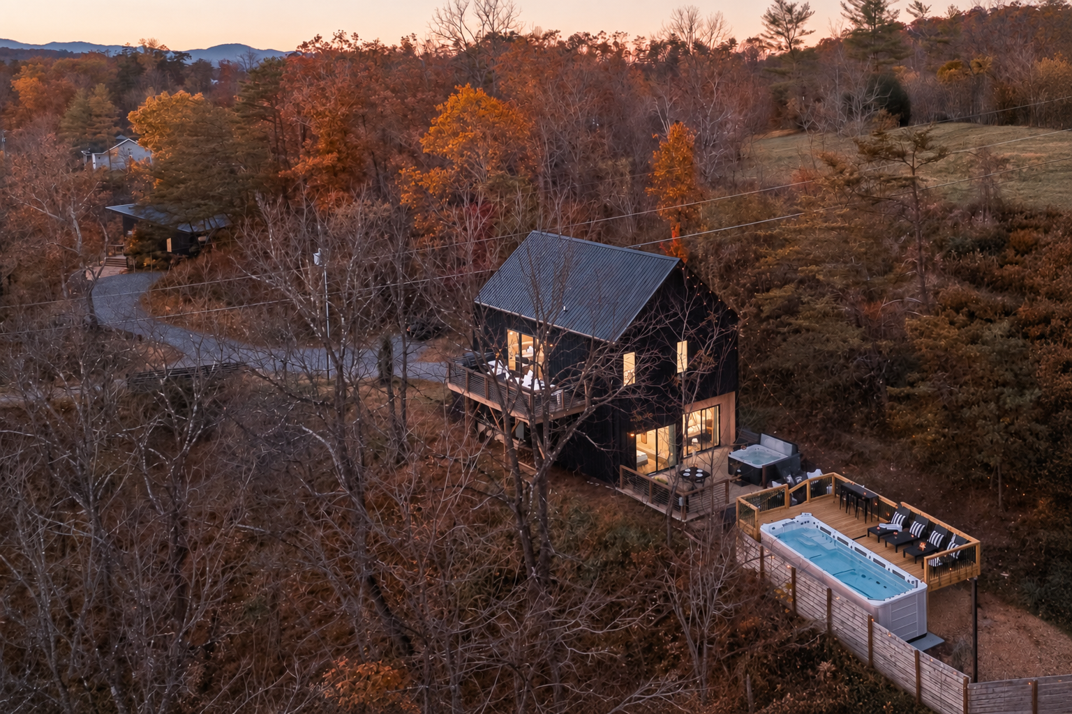 {Estate Aerial} Gallery House illuminates the hillside with warm string lights, with Glass House tucked just beyond—twin estates set amid rolling hills and Blue Ridge vistas, all moments from