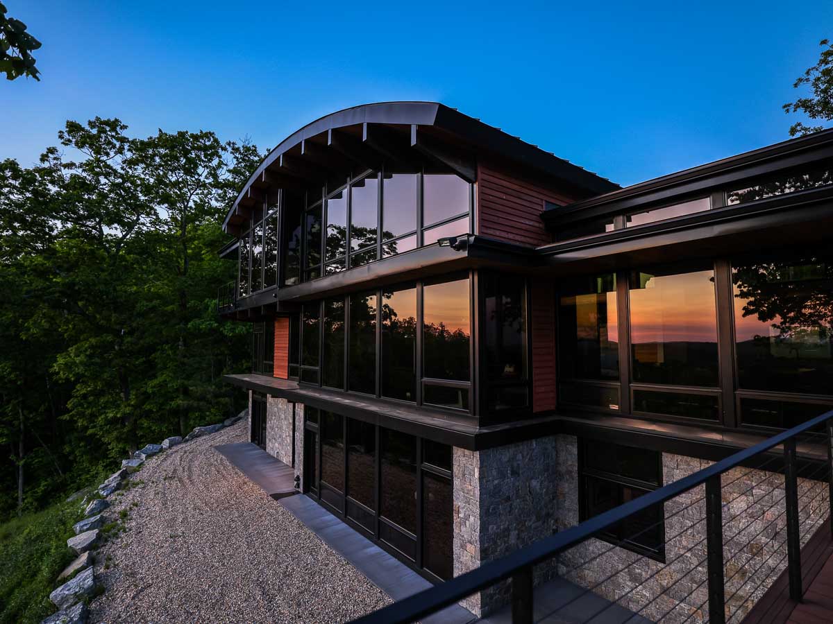 Sunset reflected across three floors of glass at the back of Sunset Falls Estate &mdash; Berkshires modern mountain home