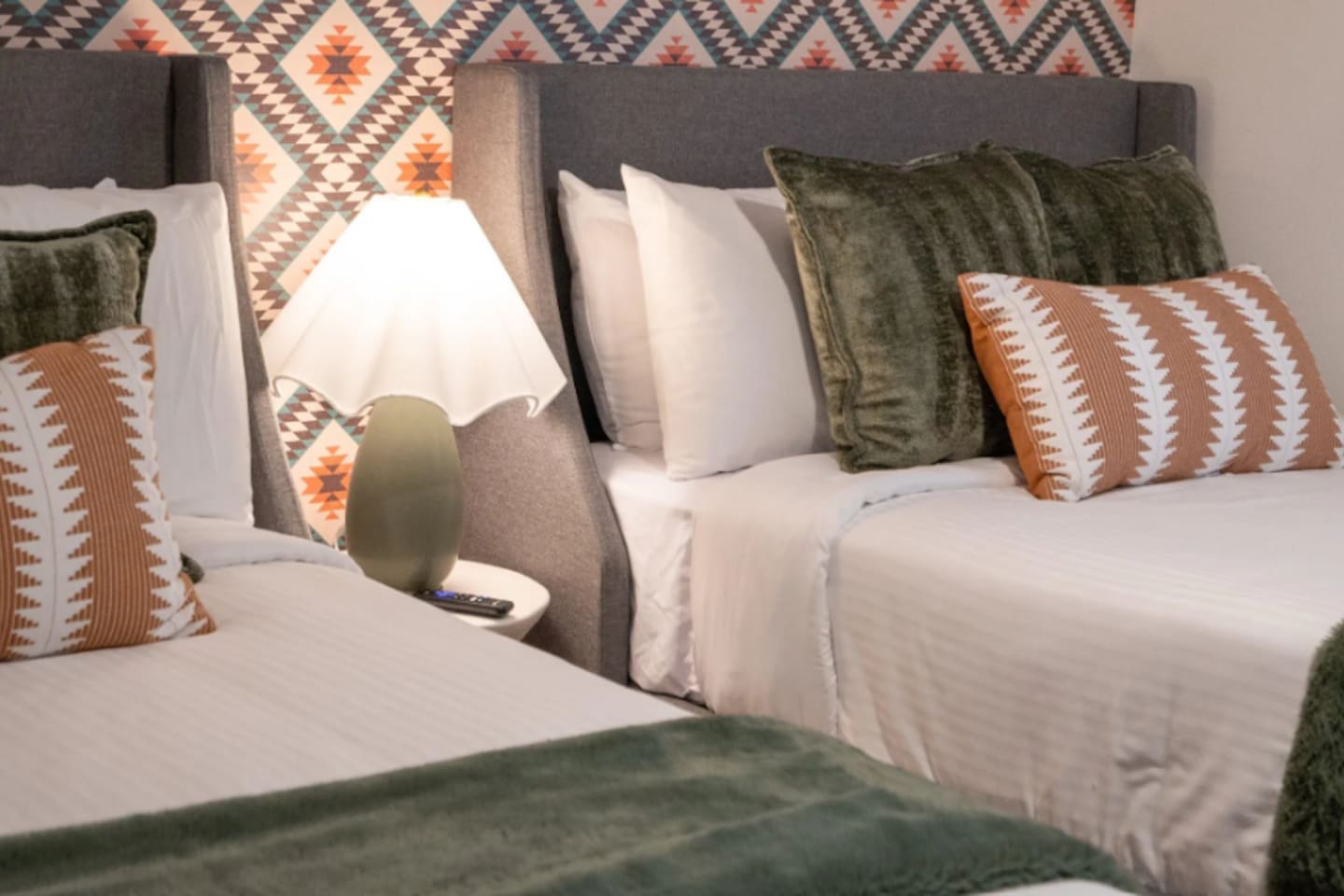 Two beds dressed in plush layered linens, set against a bold Southwest print — a room designed for kids, friends, or anyone who wants their own space.