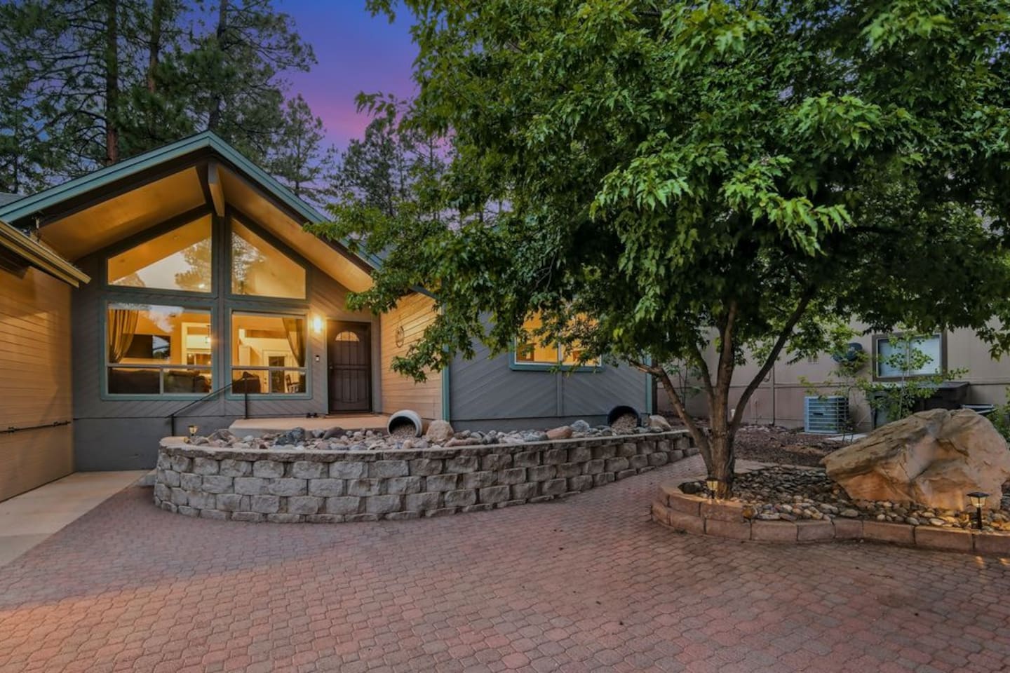 Evening courtyard view with mature trees, patio space, and warm interior lighting.