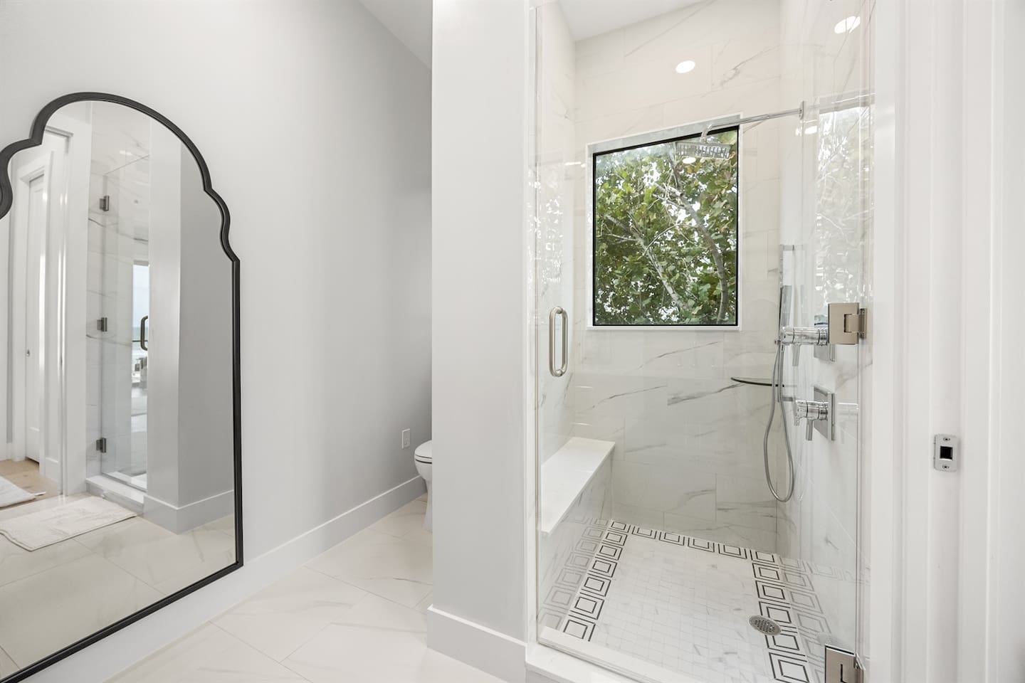 Experience luxury in this bathroom with an elegant shower featuring a sleek glass cover, a toilet nearby, beautiful flooring tiles, and a full-body mirror adding a touch of sophistication.
