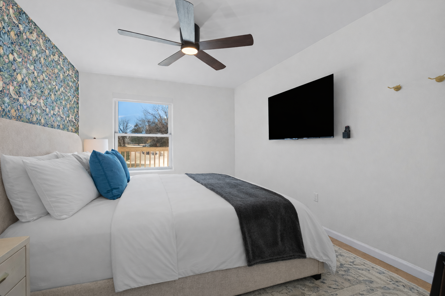 Relax in this bright bedroom featuring a plush bed, smart TV, ceiling fan, and peaceful natural light—perfect for restful nights and easy mornings.