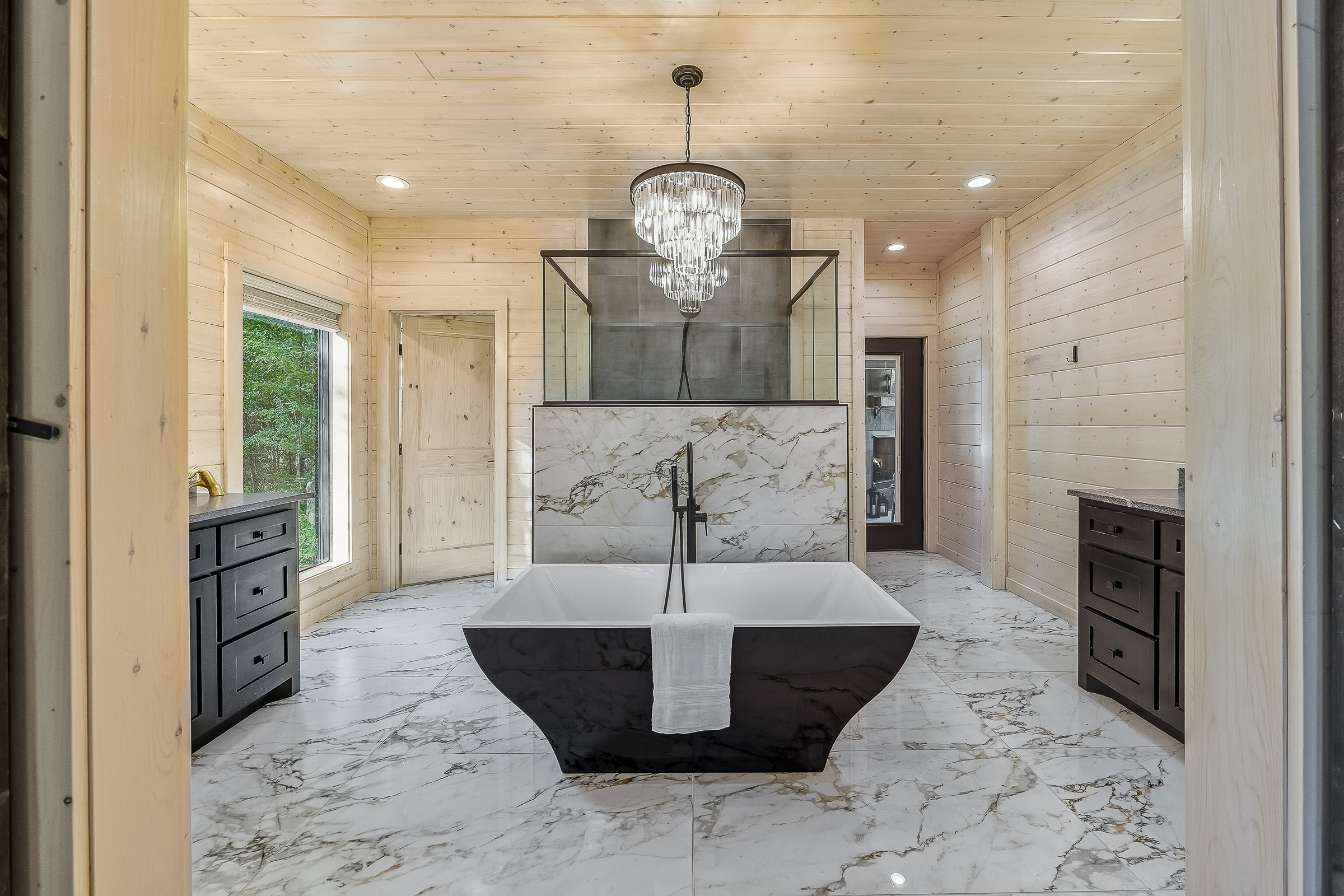 Spa level bathroom with marble inspired tile, chandelier lighting, and a deep soaking tub for total relaxation.