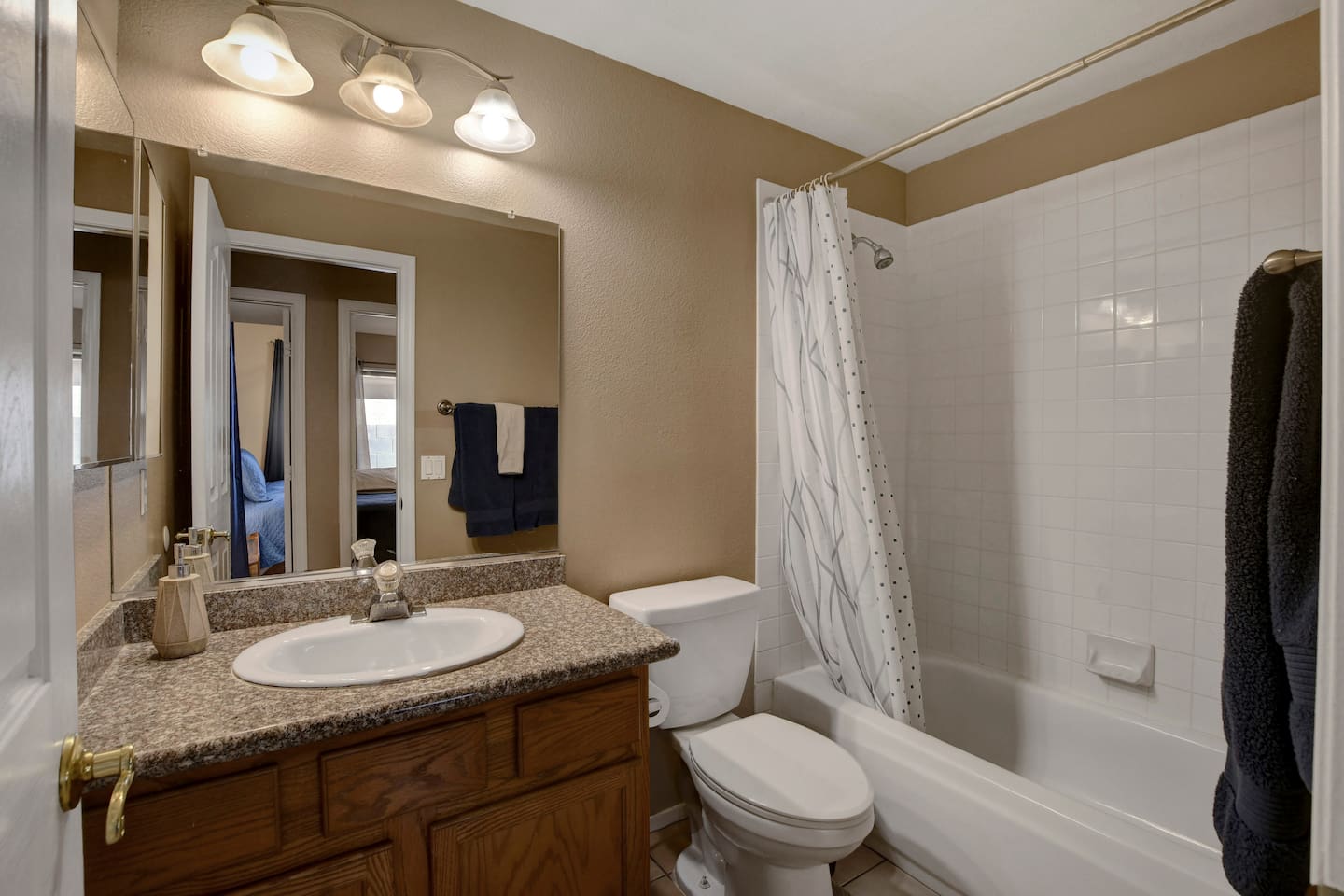 Bright bathroom with granite-top vanity, big mirror, and tub/shower combo