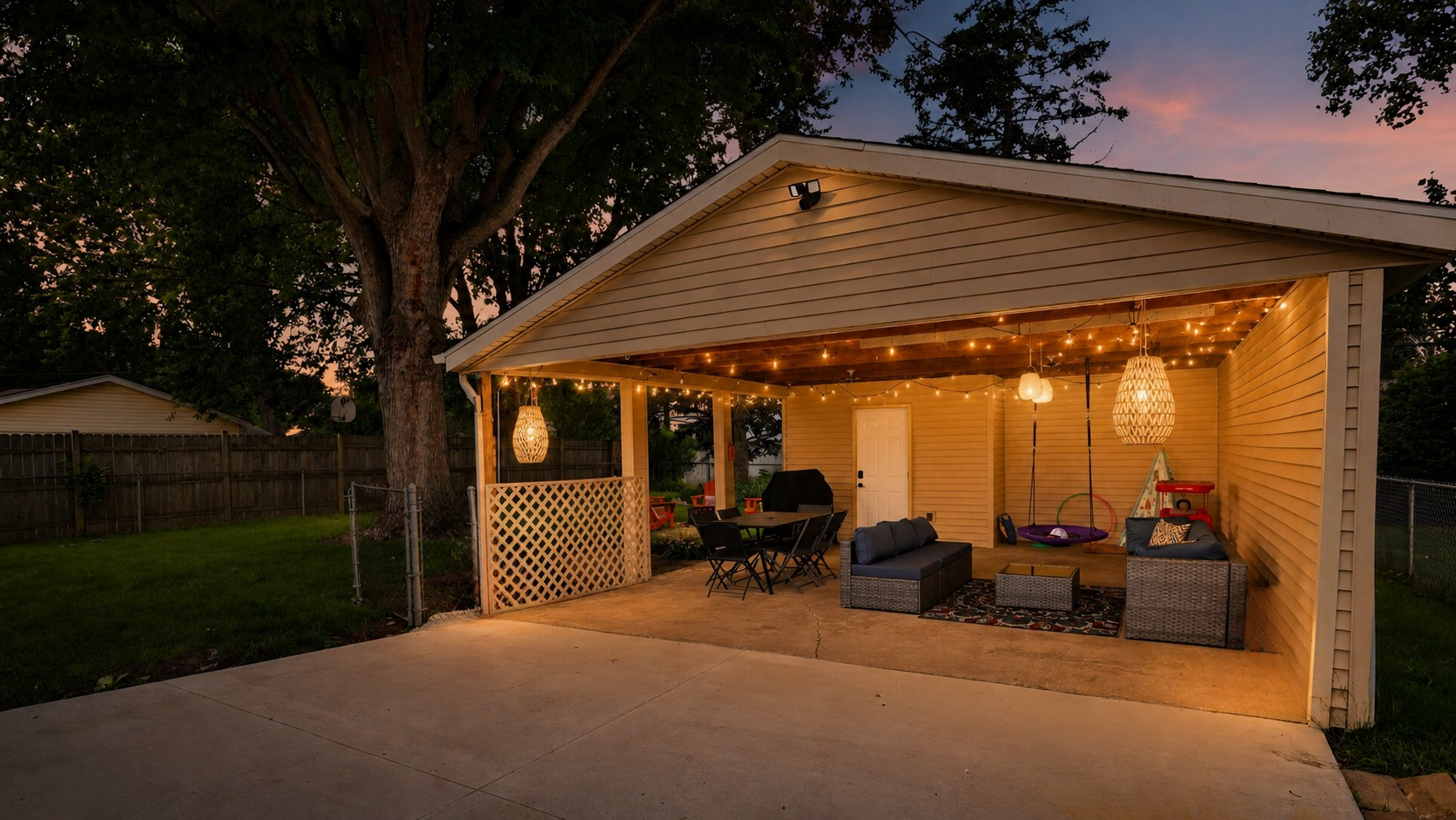 The heart of the home—our covered outdoor living room with dining, conversation seating, a family swing, and warm evening lighting.