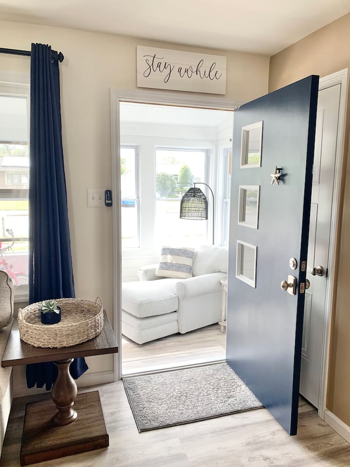 Welcome home! The navy front door opens into a bright, airy entryway that leads directly into a sun-drenched lounge area. With coastal accents and warm wood tones, it’s a beautiful first impression for your seaside getaway.