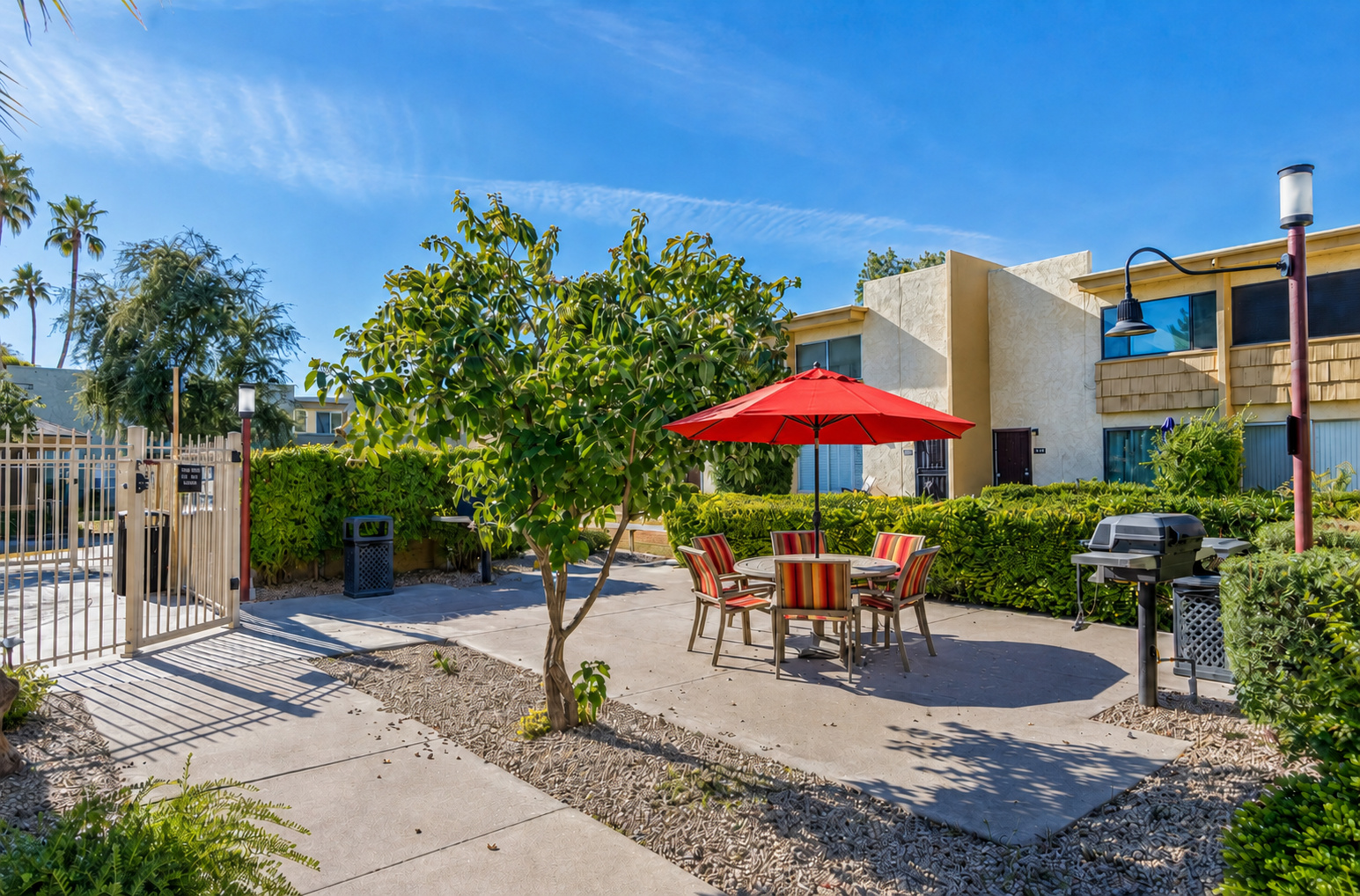 Shared outdoor dining area with a red umbrella, BBQ grill, and pool access nearby.
