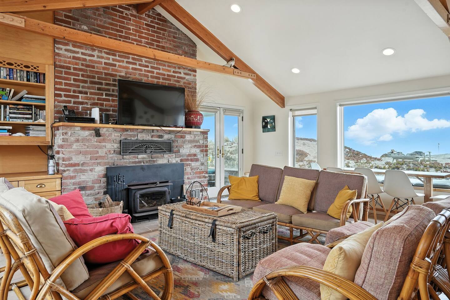 - Inviting living area with brick fireplace, flat screen TV, and rattan seating  
- Vaulted ceilings and exposed beams add rustic coastal charm to the space  
- Perfect for gathering after a day of beachside adventures  