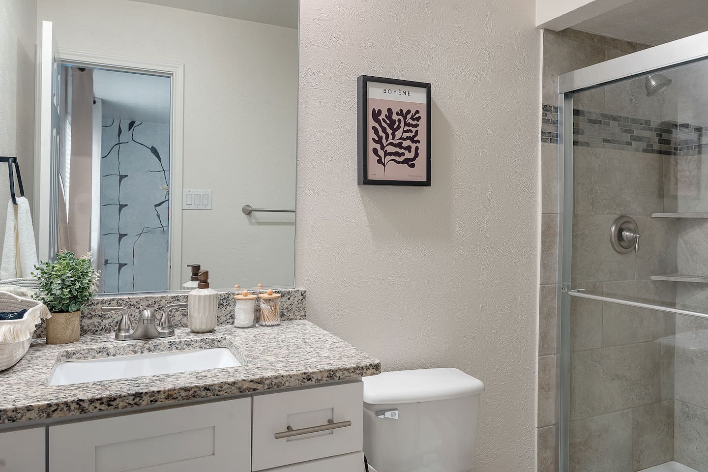 This modern bathroom features a granite countertop and a spacious shower. Thoughtful decor and essential amenities create a welcoming space.
