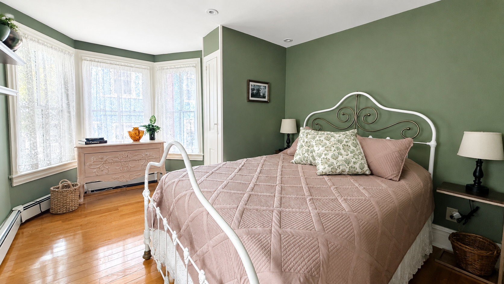 A queen bedroom on the second floor with original hardwood floors, a bay window dressed in lace, and that particular quiet that only old houses have.