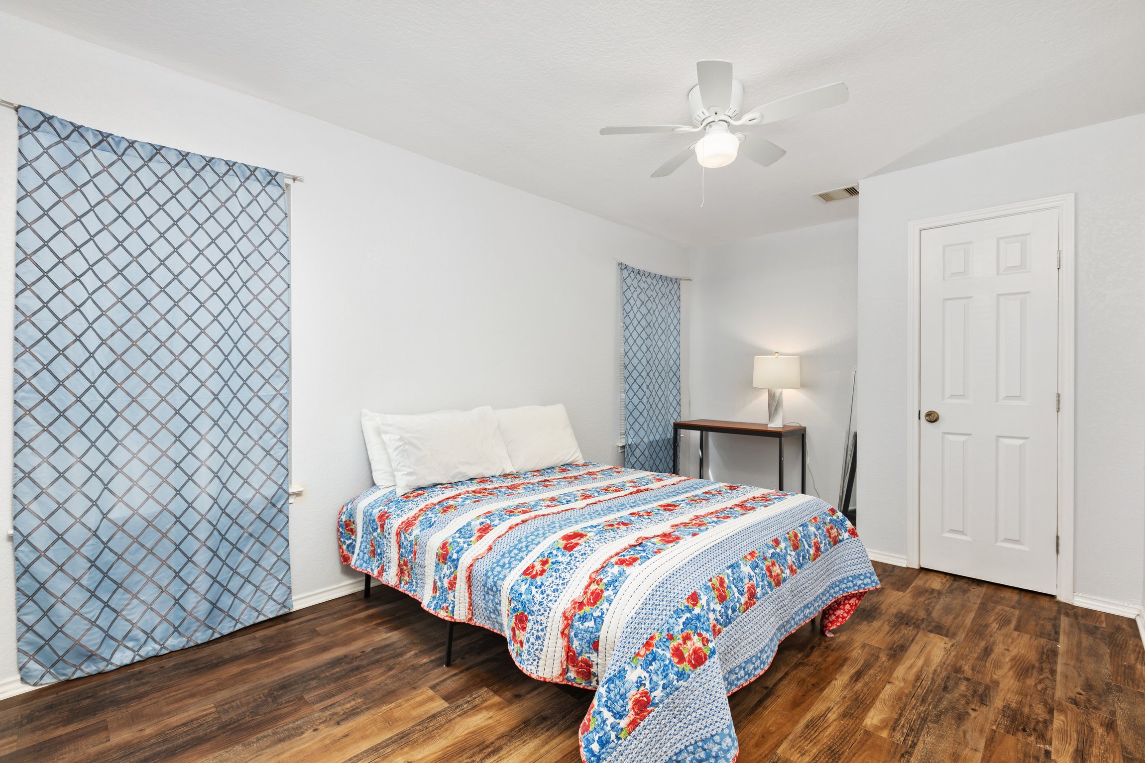 Queen bedroom with colorful bedding, ceiling fan, and hardwood floors. Hotel-quality linens, clothing storage, room-darkening shades, and extra pillows and blankets included. Current decorative blankets, bedding, and wall art are not shown in these photos.