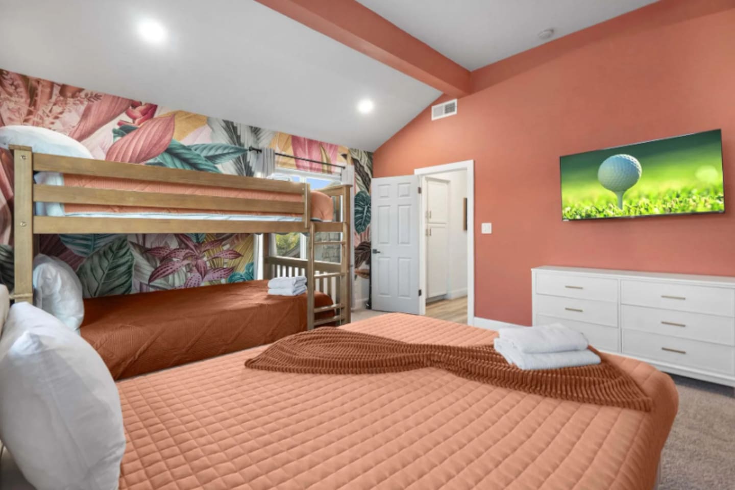 Colorful guest bedroom with queen bed, bunk beds, and vibrant botanical wallpaper.