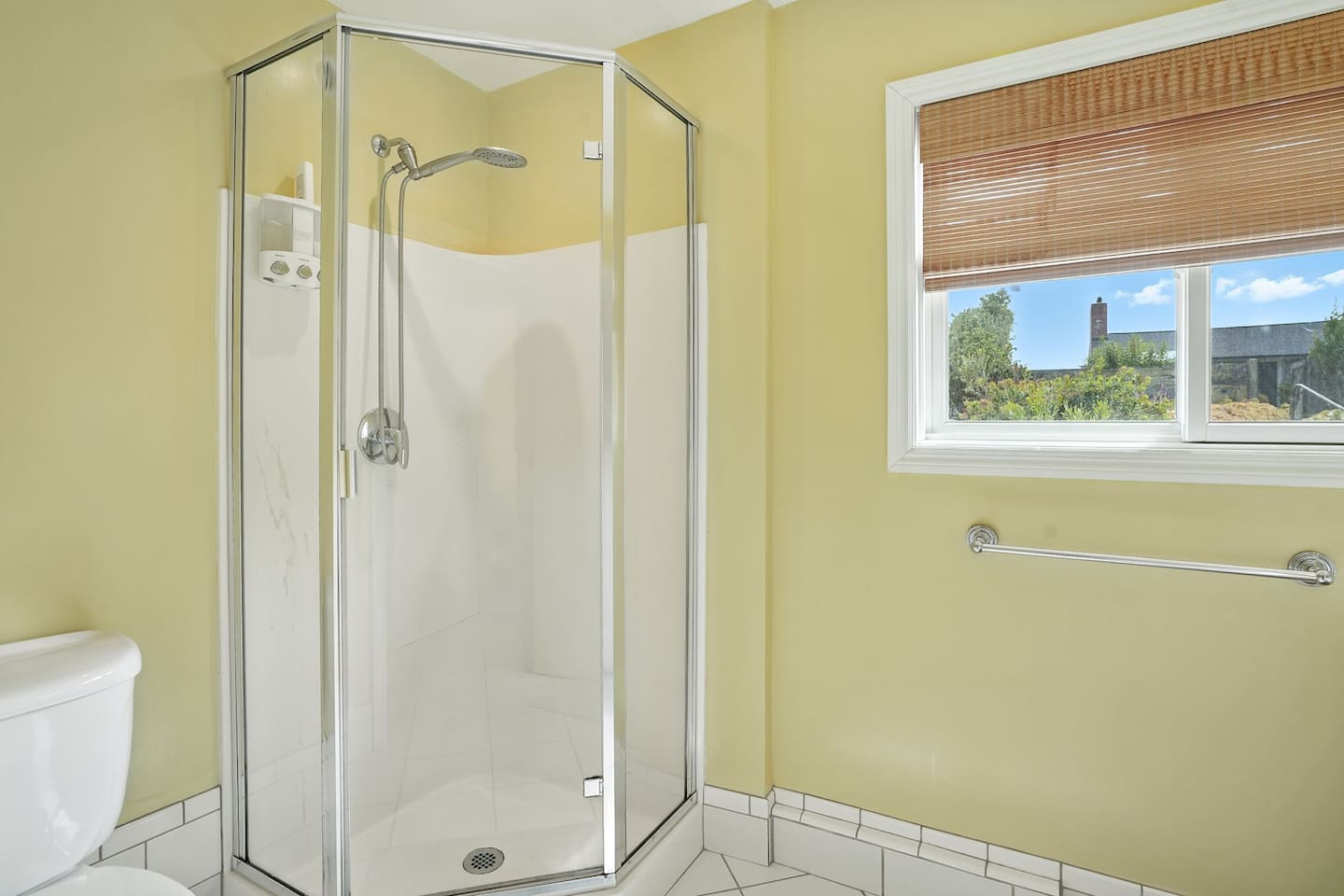 - Bright bathroom with corner glass shower and sleek fixtures for a modern touch  
- Window with bamboo shade allows soft daylight while maintaining privacy  
- Light yellow walls create a cheerful and inviting atmosphere
