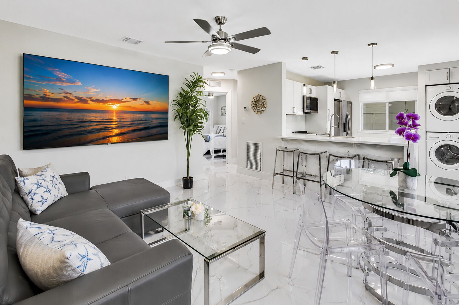Open-concept living and dining area with a comfortable sectional, 65” Smart TV, dining table, breakfast bar seating, and direct access to the fully equipped kitchen.
