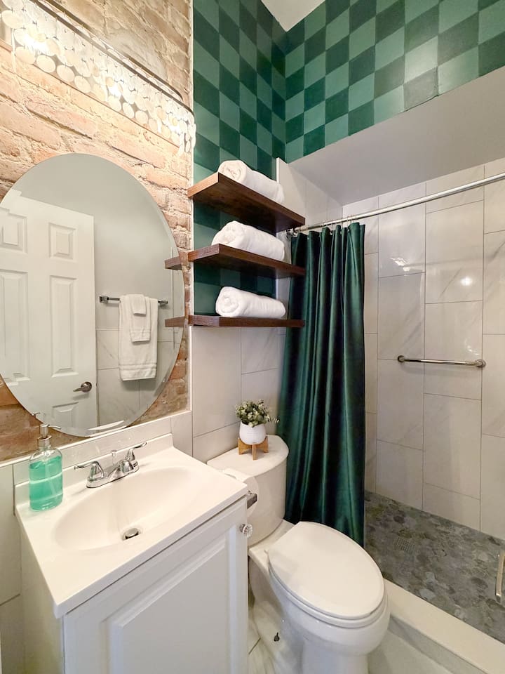 Accessible from the whole house via the kitchen, the hallway bathroom features exposed brick, emerald checkerboard walls, and spa-style walk-in  shower. Fresh towels and essentials provided for a comfortable New Orleans stay. 
