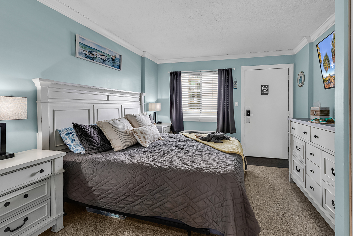 Spacious king bedroom with dual nightstands, coastal blue walls, and flat-screen TV — sleep comfortably after a day at the beach