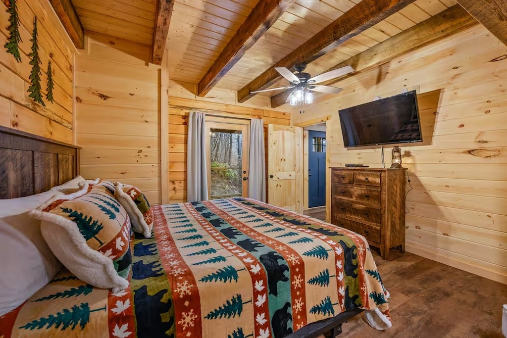 The main level king bedroom at Bear Paws Cabin offers parents a private retreat with an attached full bathroom &mdash; no sharing with the kids. Rustic log cabin d&eacute;cor, hardwood floors, and warm lighting create the cozy Smoky Mountain atmosphere families love
