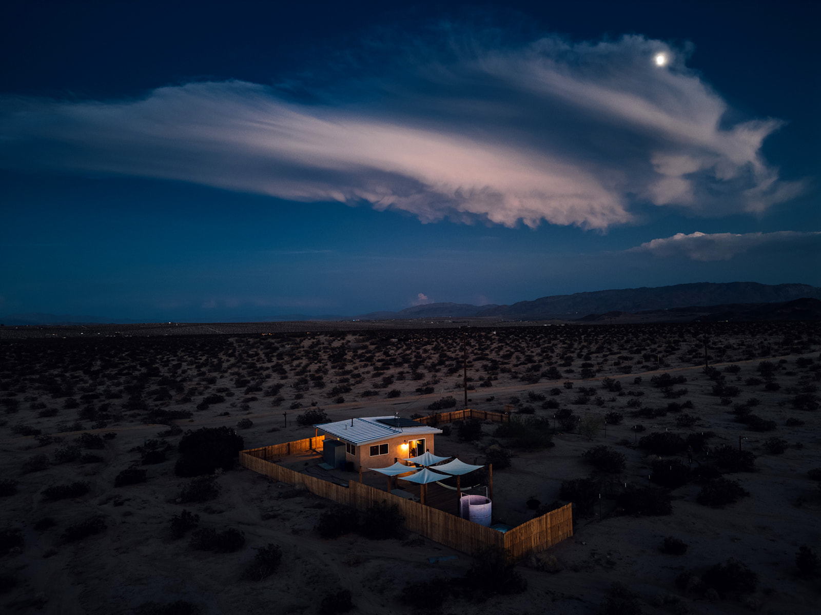 Stunning aerial night shot of Pink Moon cabin glowing under the desert sky, surrounded by peaceful open landscape and moonlight.