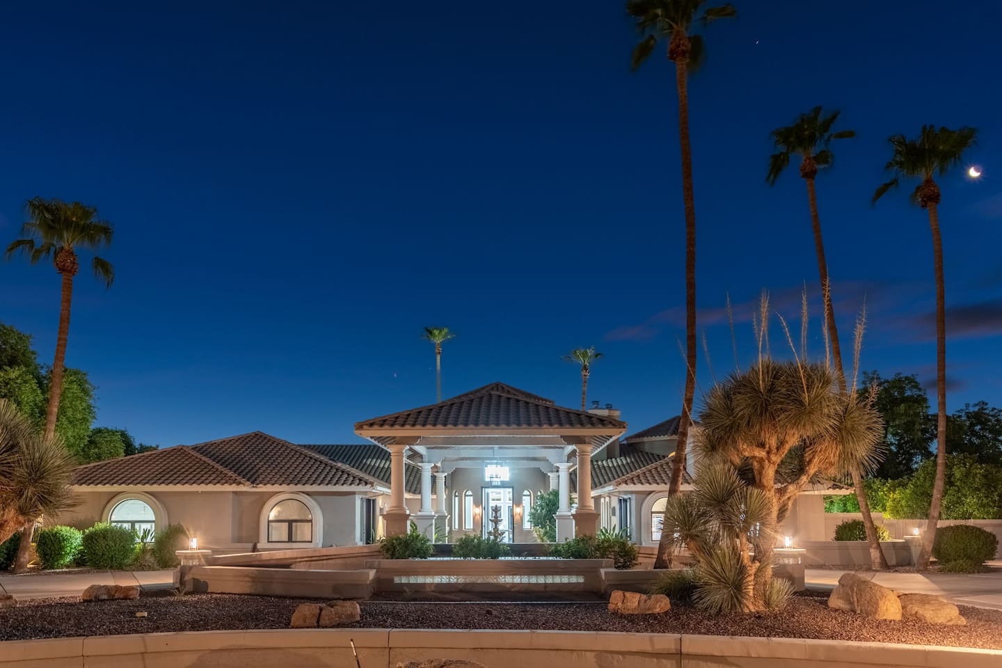 A breathtaking view of the estate illuminated under a desert night sky—complete with palm trees and elegant architectural symmetry.


