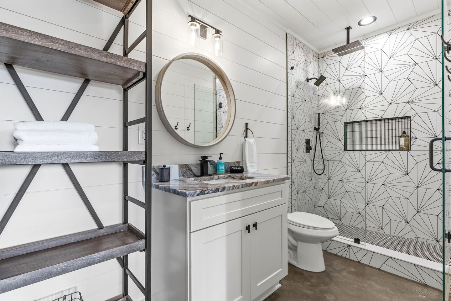 Step into this stunning modern bath with concrete flooring, oversized mirror, and eye-catching geometric tile shower. Luxurious rainfall + showerhead + handheld sprayer create a true spa feel, with open industrial shelving for towels and extras.