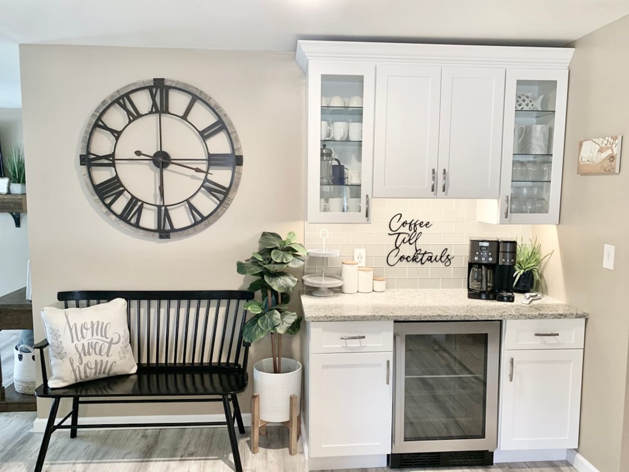 Start your morning or end your evening at our dedicated beverage bar. Features a drip coffee maker, wine cooler, and "Coffee Till Cocktails" decor. A charming black bench and oversized wall clock complete this stylish and functional nook.