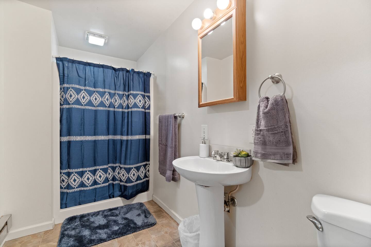 Modern full bathroom featuring a sleek sink with faucet, a stylish mirror, a spacious shower, a toilet, elegant white walls, and polished flooring—designed for comfort, functionality, and a clean, inviting atmosphere