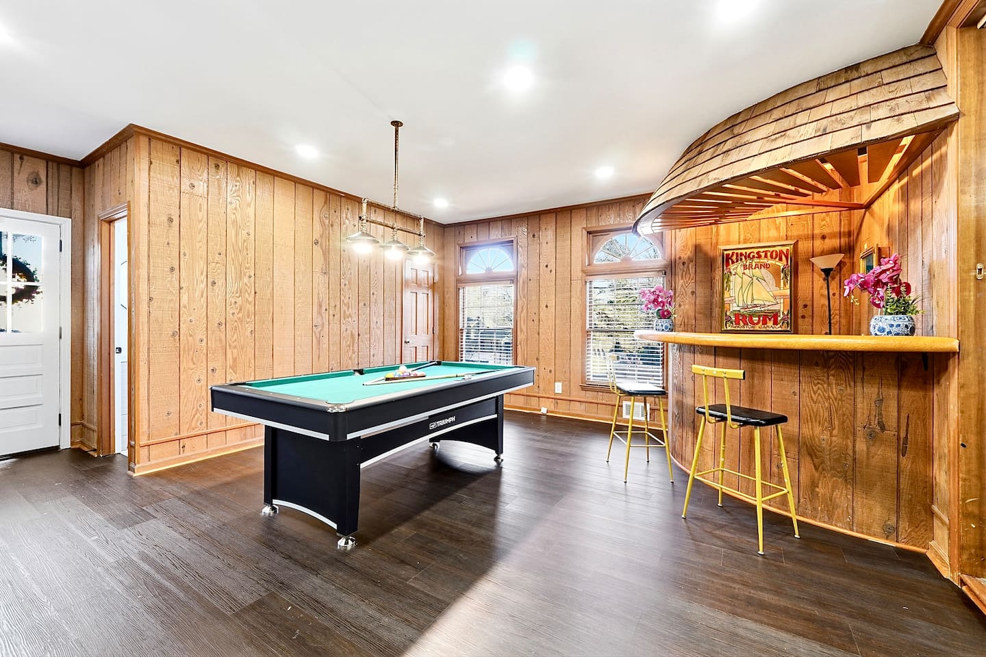 Enjoy this main-floor game room near the side entrance featuring a convertible pool and ping-pong table, a custom curved wood bar, and a Roku powered smart TV—ideal for entertaining and casual gatherings.