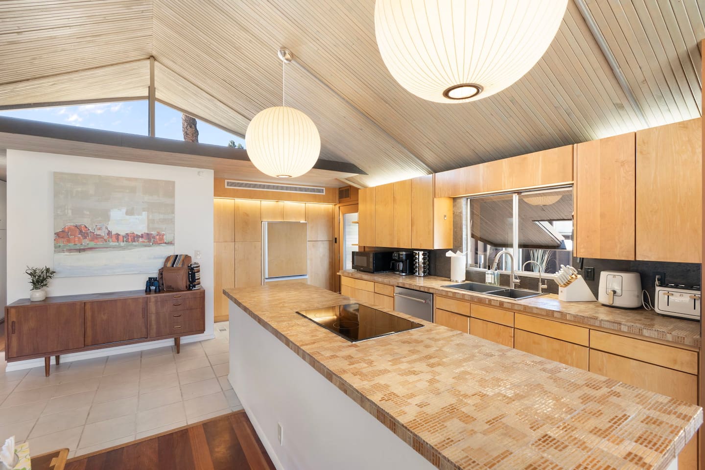 Modern open kitchen with warm wood cabinetry, oversized island cooktop, and soaring vaulted ceilings filled with natural light.