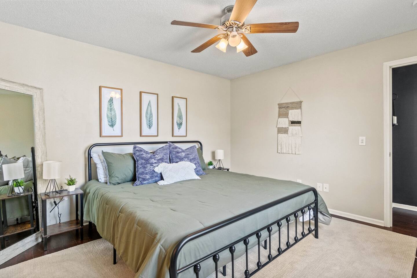 Relax in this thoughtfully designed bedroom with warm wood flooring, a ceiling fan for comfort, and tasteful botanical artwork.
