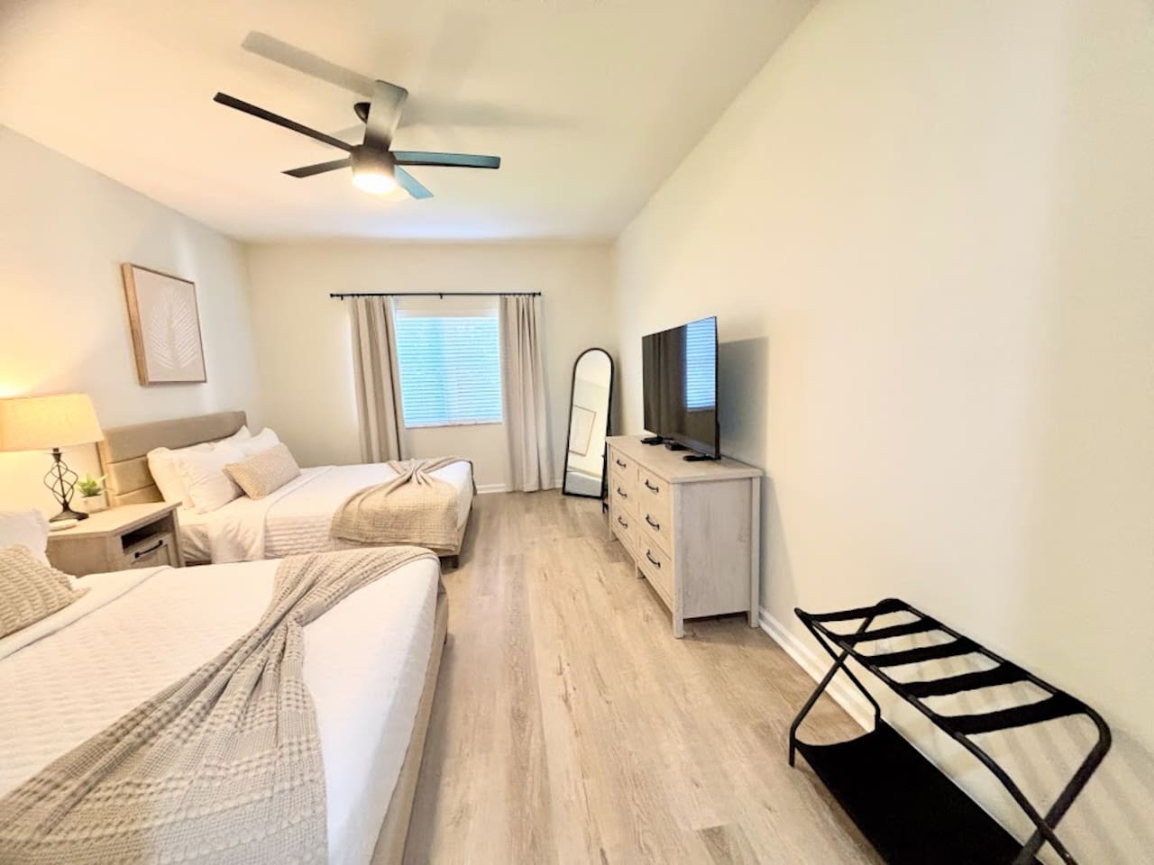 Spacious bedroom with two comfortable beds, wood-look flooring, ceiling fan, TV, dresser storage, and a convenient luggage rack.