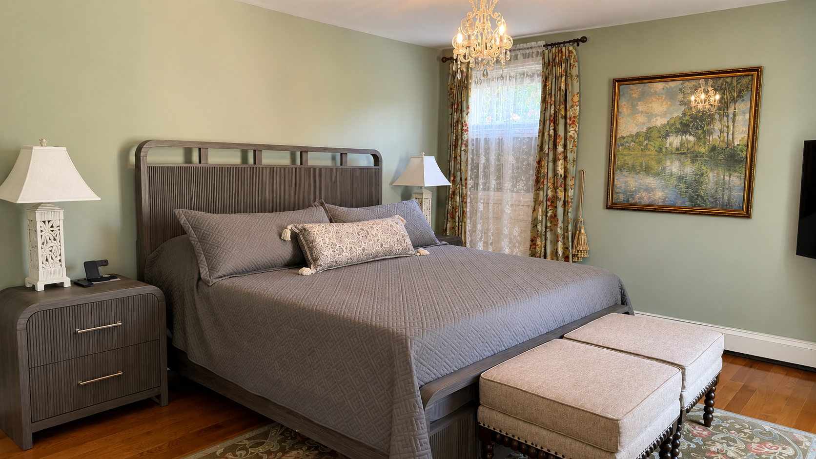 The primary suite — a king bed, crystal chandelier, hardwood floors, and an en suite bath. The floral drapes and lace sheers are a nice nod to the Victorian bones of the house.