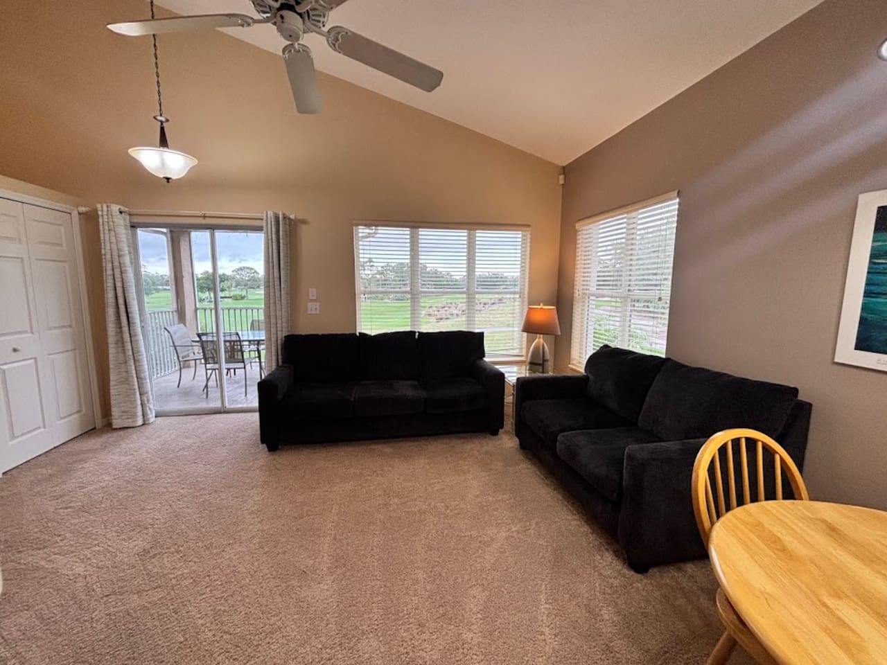 Spacious living area with comfortable seating, ceiling fan, large windows, and direct access to the private screened balcony.
