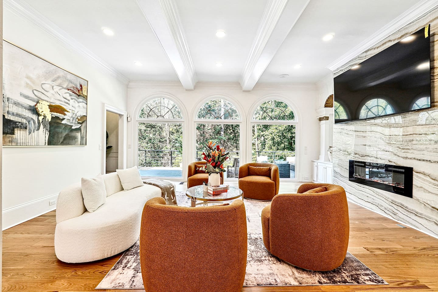 Located straight ahead from the front entry, this main-floor living room showcases a striking modern design with a round shaped contemporary sofa, four orange accent chairs, a smart TV, and a fireplace for a warm, elevated lounge experience.