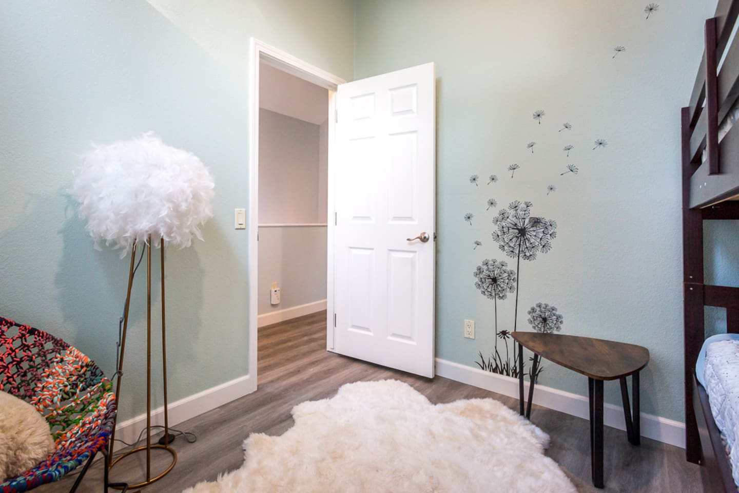 - Charming bedroom corner with playful dandelion wall decal adding visual appeal
- Fluffy chair and soft area rug create a relaxing and comfortable reading nook
- Light green walls and wood look flooring keep the space fresh and inviting