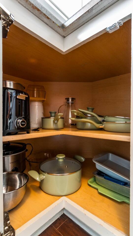 A peek inside the cabinet reveals a full set of cookware, mixing bowls, a toaster, popcorn maker, and crockpot—all ready for your culinary adventures.