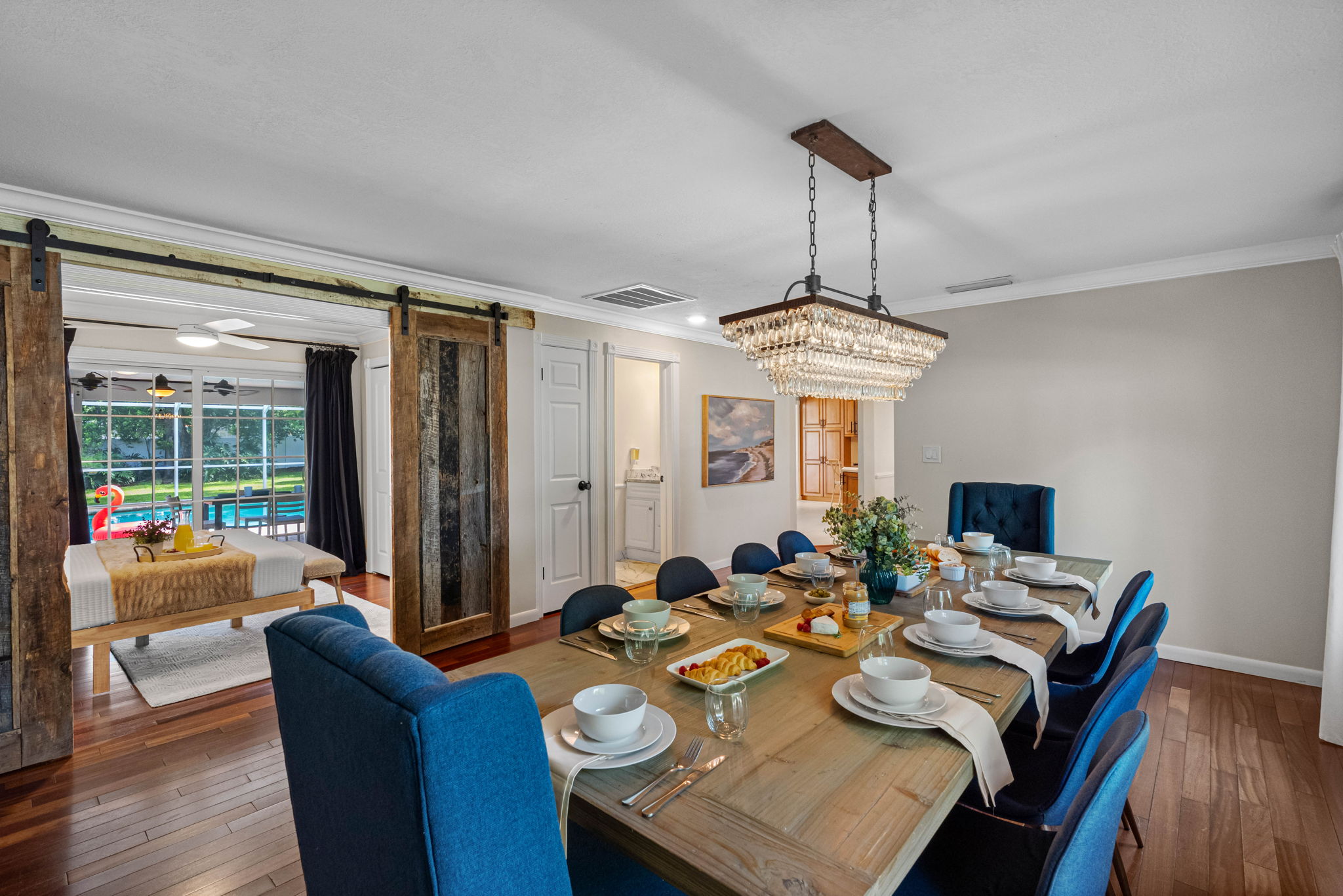 Elegant dining room featuring a rustic wood table, plush blue chairs, and a sparkling chandelier centerpiece.