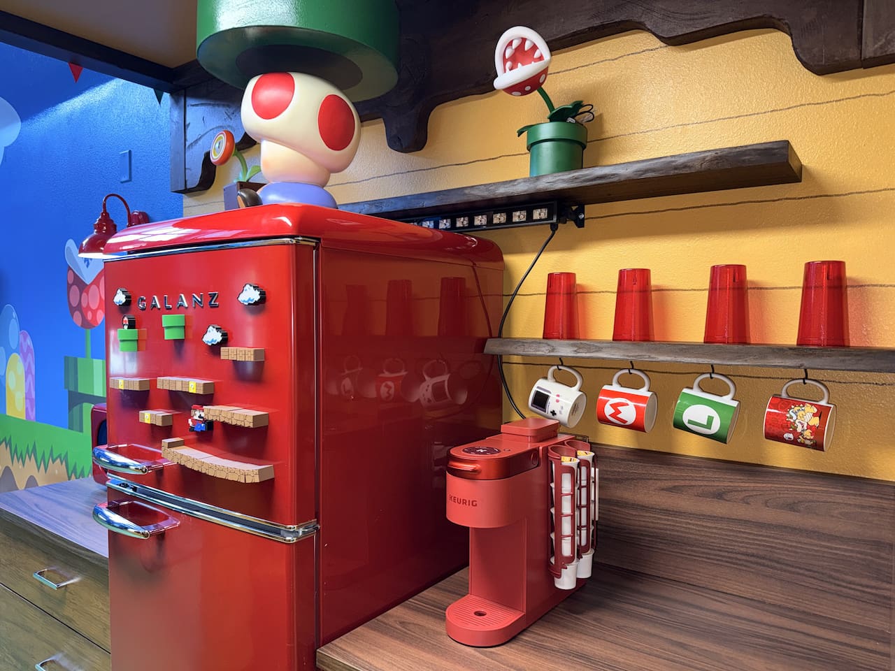 Retro red fridge and coffee station at Mario's Mini Mansion in Clermont, FL! Toad peeking over the top, colorful hanging mugs, and playful Super Mario accents bring joy to every morning brew and snack time.