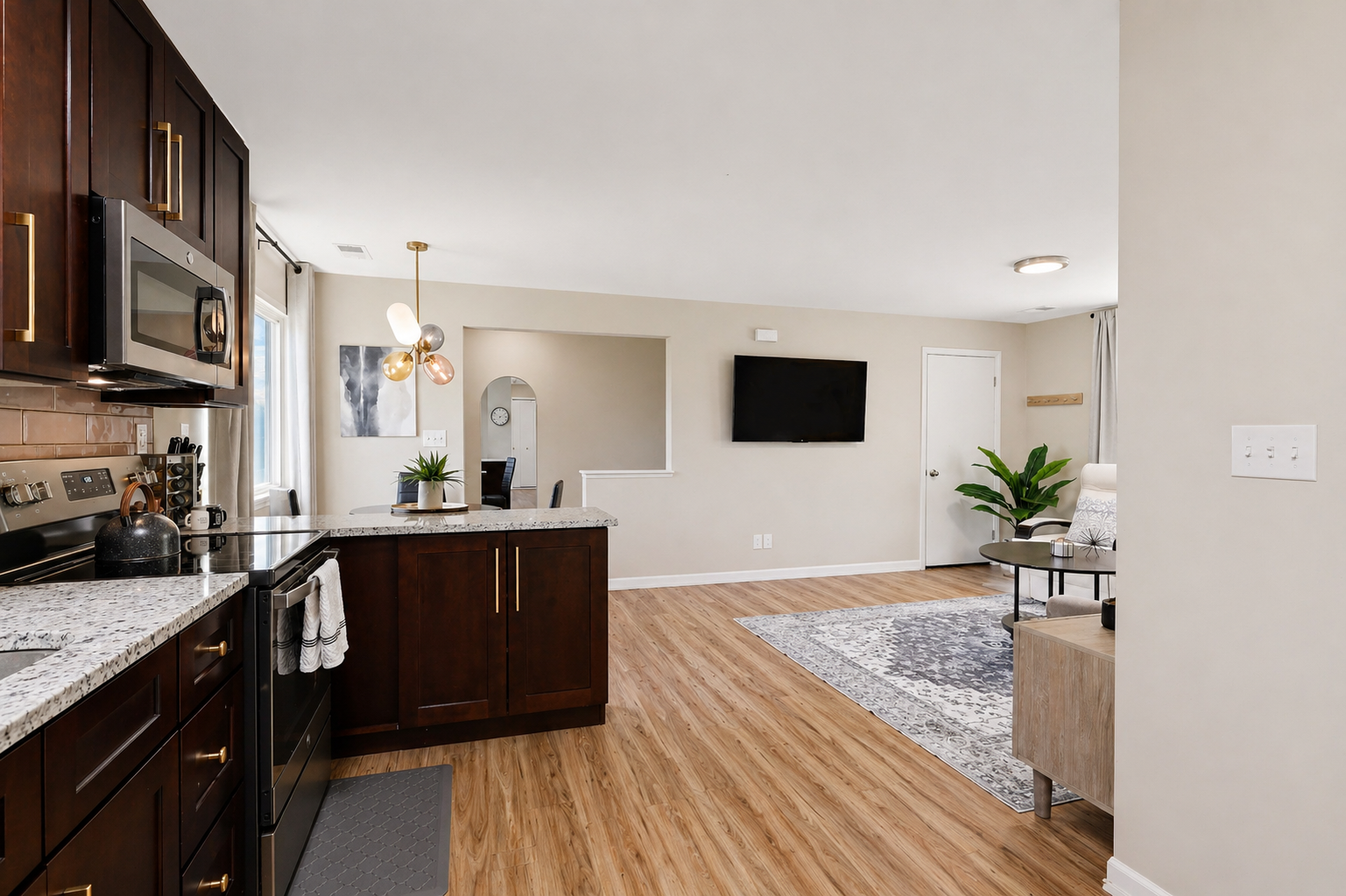 Discover a well-appointed kitchen with warm wood flooring. This indoor space offers a clean and modern design, complete with a countertop, cabinetry, sink, and essential kitchen appliances. Enjoy meals at the table and relish the inviting ambiance created