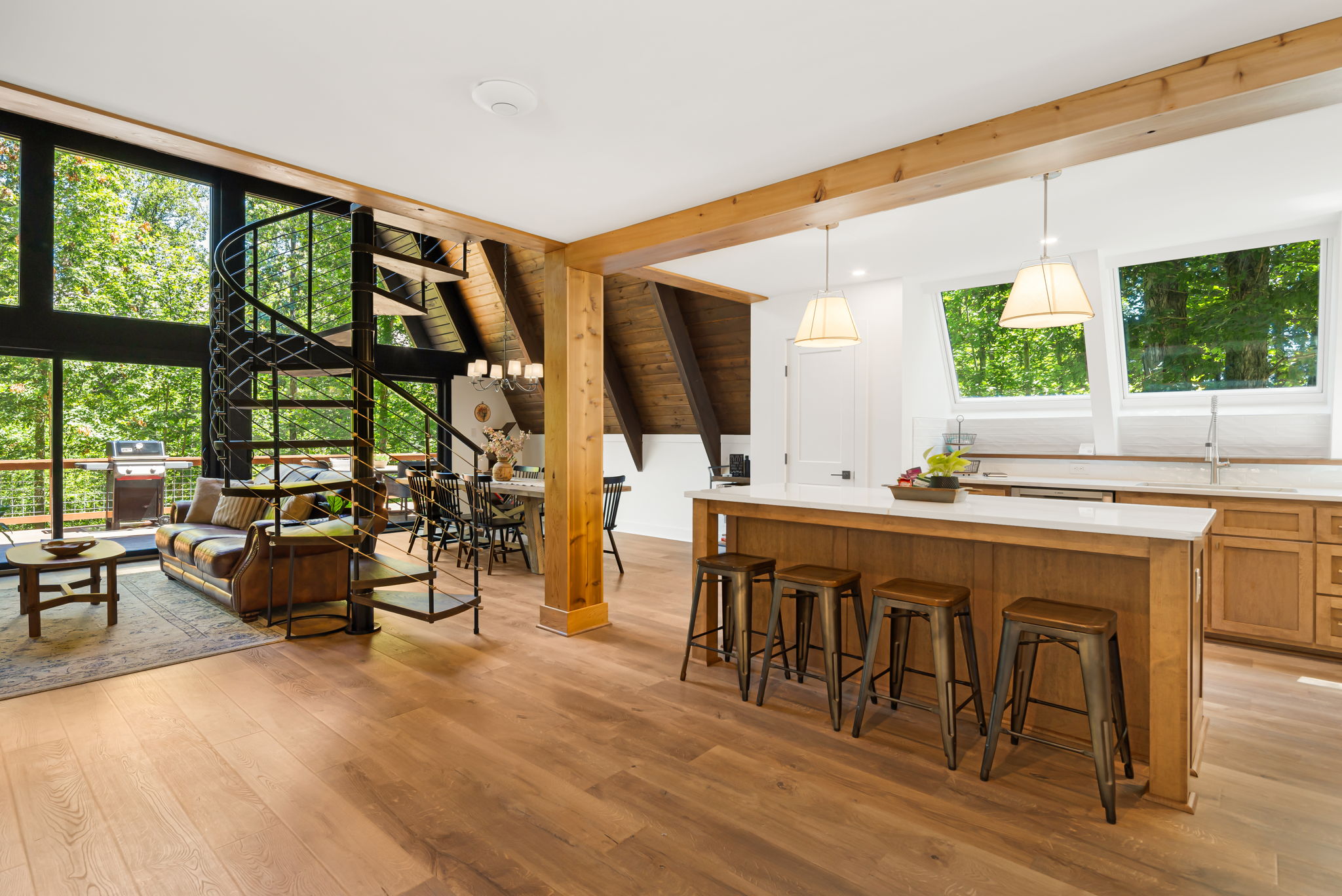 An open floorplan flooded with natural light from the kitchen skylights or the bank of windows in the living room. This view shows spiral staircase to the second floor, the living room with comfortable seating as well as a dining room with seating for 8.