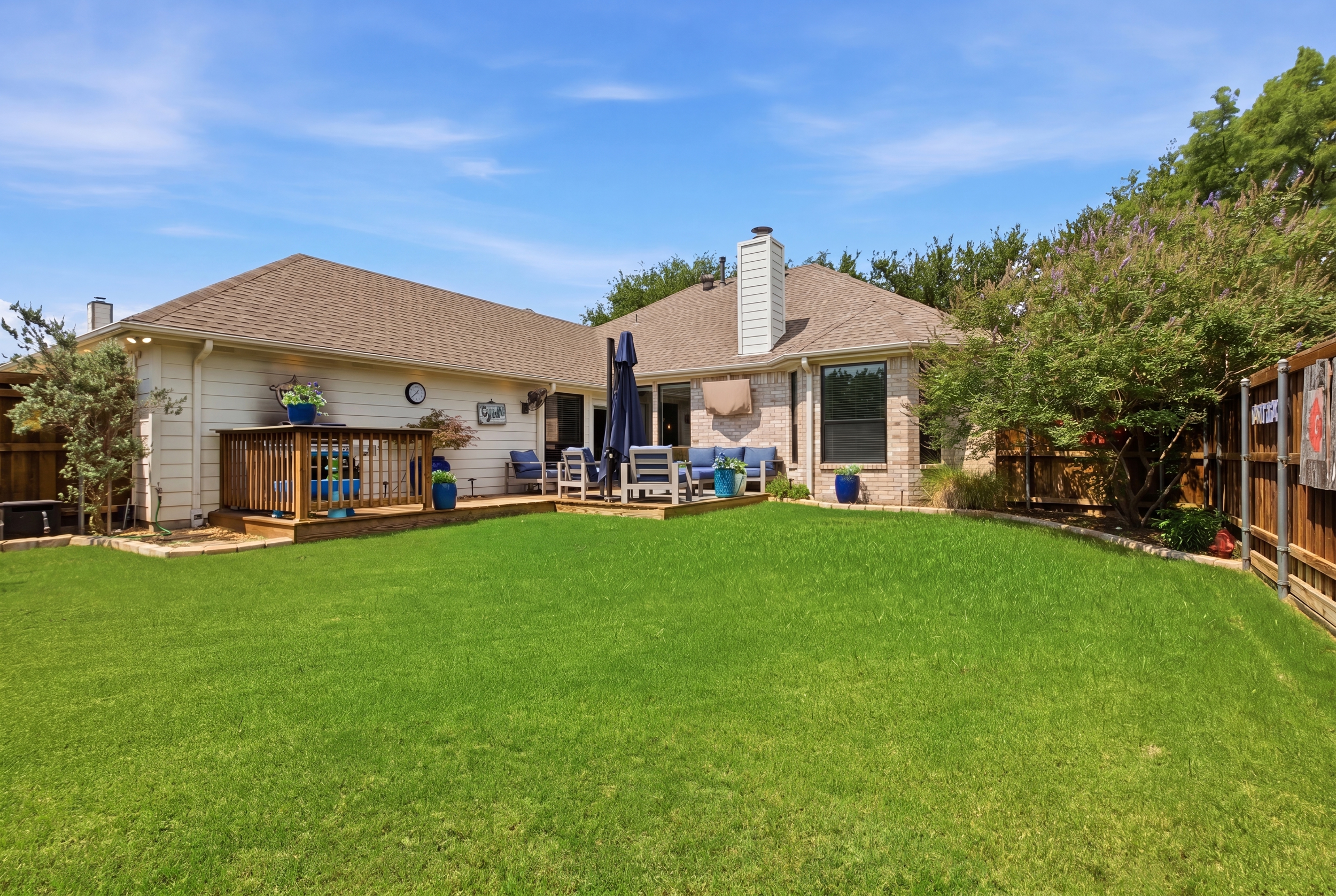 Spacious lawn and wooden Patio with comfortable Outdoor Furniture, navy cushions, and a large umbrella. Ideal for morning coffee or evening grill-outs near Grandscape and Frisco.