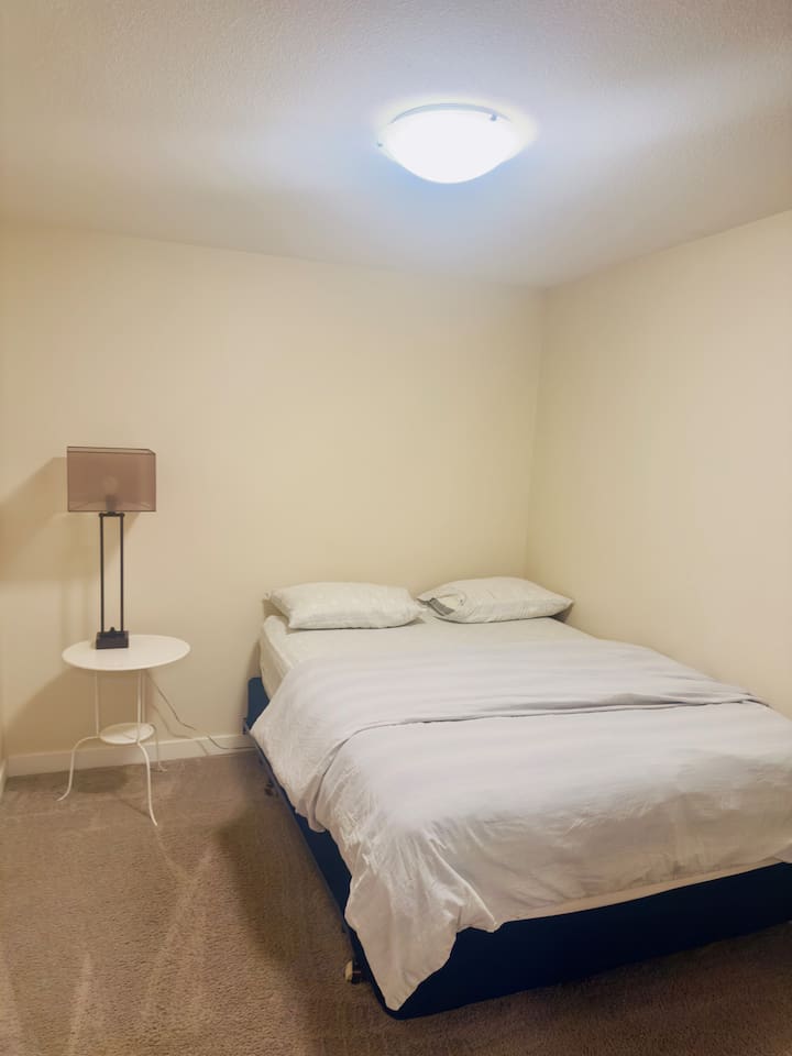 Cozy minimalist bedroom with queen bed, soft lighting, clean comfort.