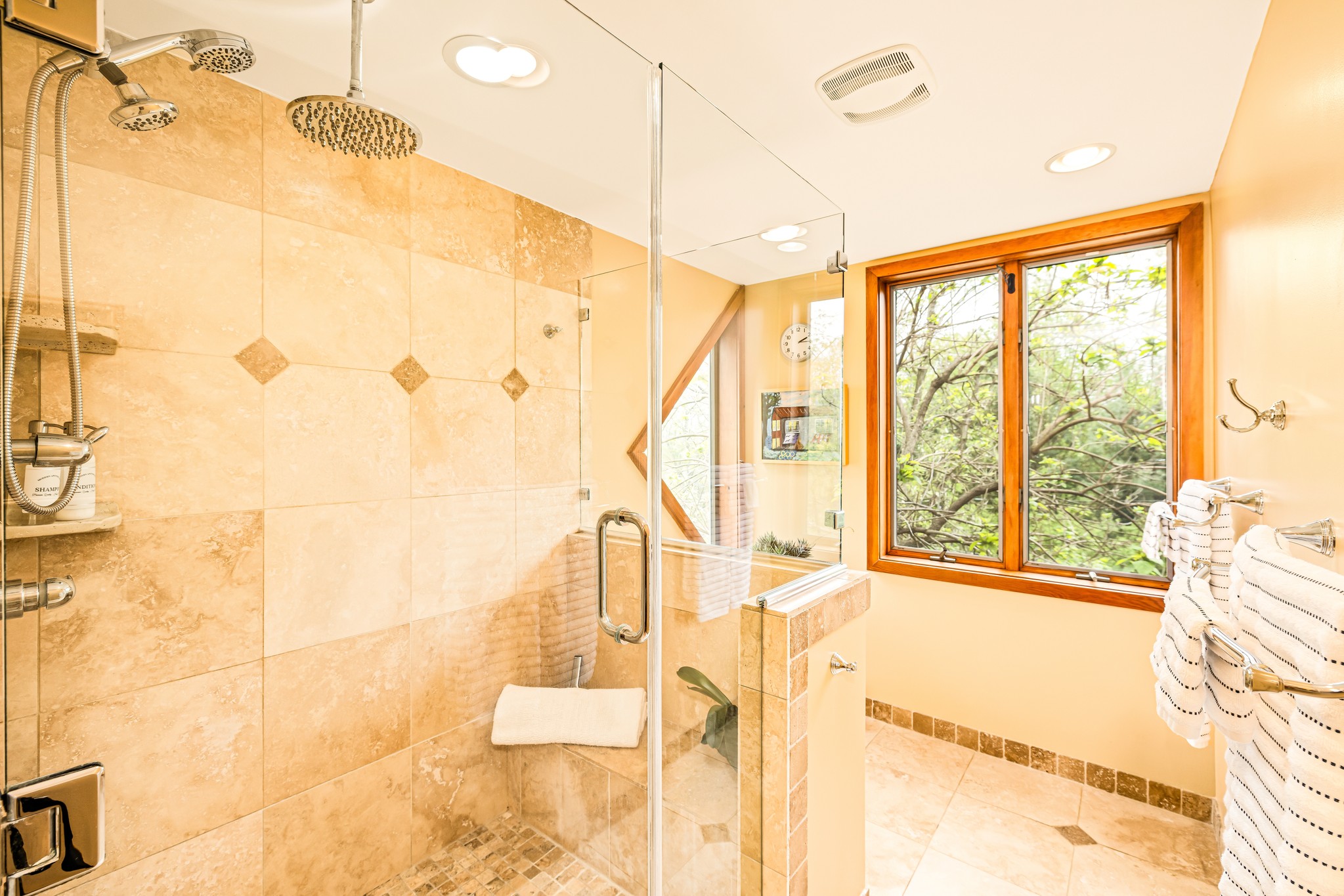 A true spa retreat: The primary bath with walk-in shower, dual rainfall heads, and a built-in bench. Enjoy the peaceful forest views for a calm start or end to your day.