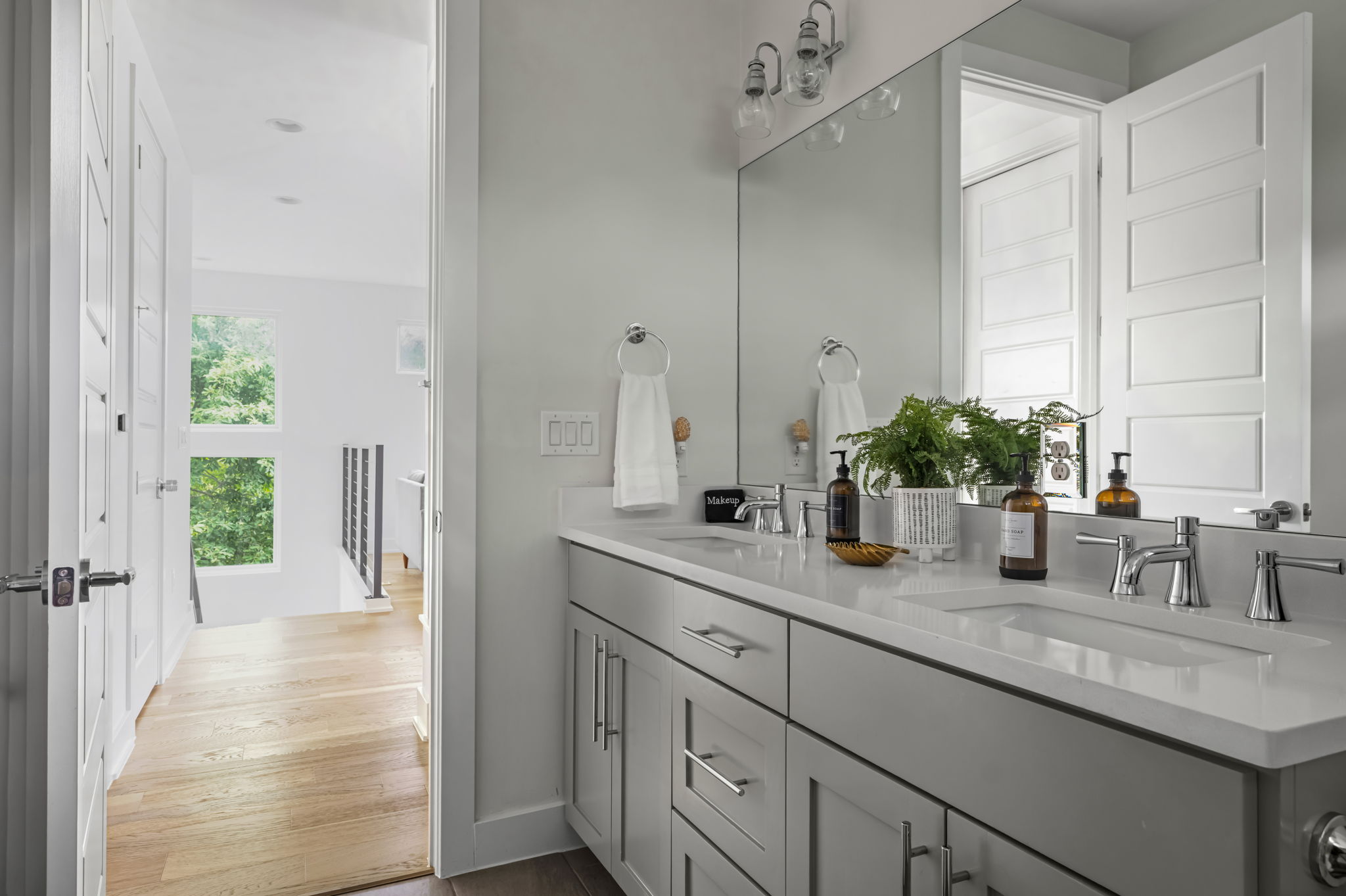 Bright ensuite vanity area with dual sinks, designer fixtures, and a view of the greenery outside.