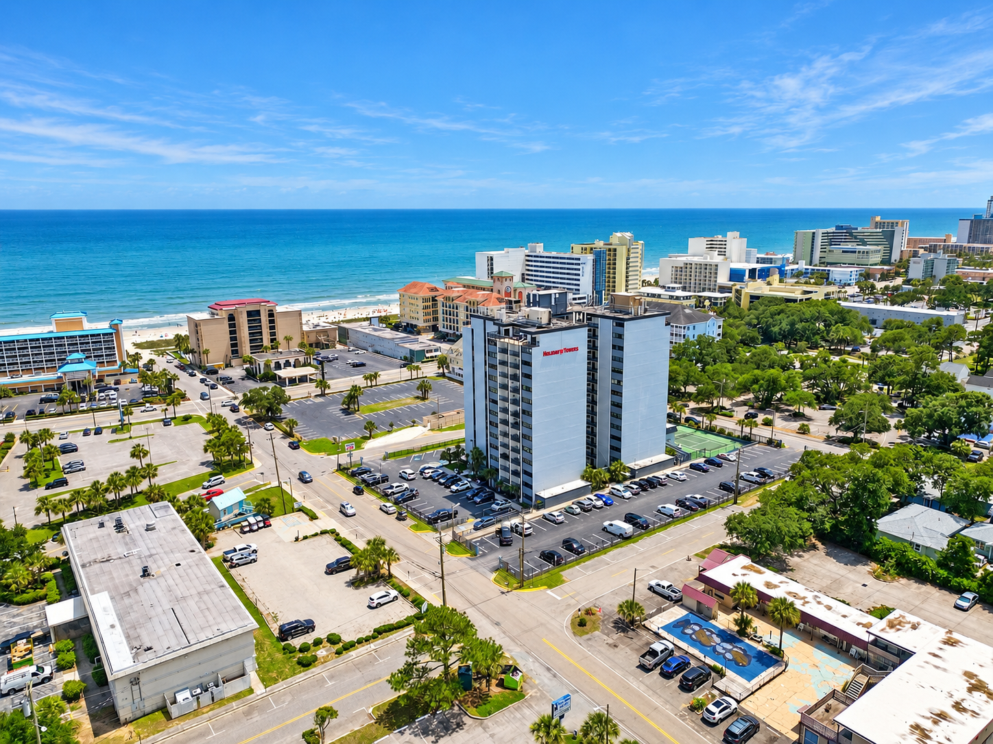 Aerial view of Holiday Towers with shared pool, hot tub, sports court, parking, and Myrtle Beach attractions nearby.